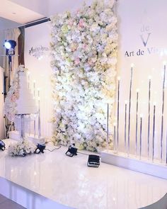 a white table topped with lots of flowers next to a tall wall covered in candles