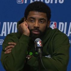 the basketball player is sitting in front of a microphone with his hand on his chin