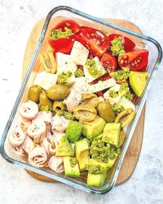 a glass dish filled with assorted vegetables and meats on top of a wooden cutting board