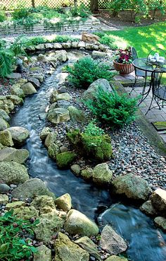 a small backyard with rocks and water running through the center, surrounded by greenery