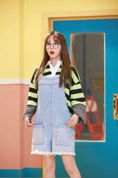 a girl with glasses and overalls standing in front of a door