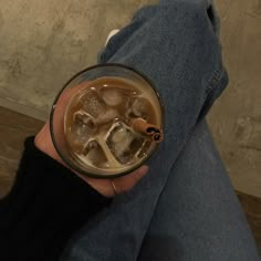 a person holding a glass filled with liquid and ice cubes on top of their legs