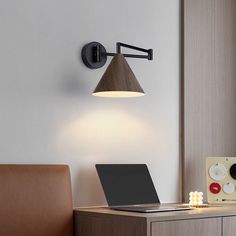 a laptop computer sitting on top of a wooden desk next to a wall mounted light