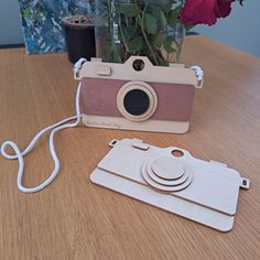 an old camera sitting on top of a wooden table next to a vase with flowers