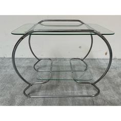 a glass and metal table with two shelves on the bottom, one shelf is empty