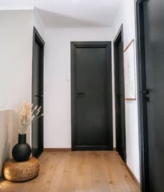 an empty hallway with two black doors and a vase on the floor next to it