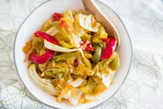 a white bowl filled with food on top of a table next to a wooden spoon