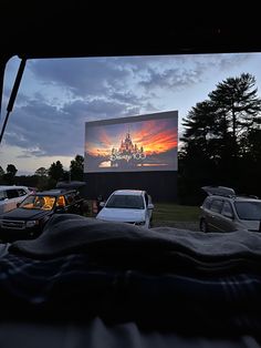 cars are parked in front of a movie screen at dusk with the sun going down