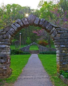 a stone arch in the middle of a grassy area