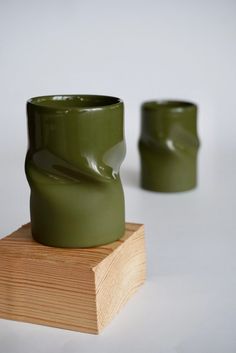 two green vases sitting next to each other on a wooden block in front of a white background