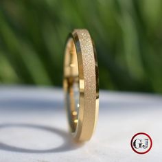 a gold wedding ring sitting on top of a white cloth covered table with grass in the background