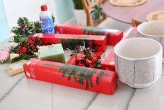 several wrapped presents sitting on a table next to two mugs and some other items