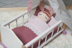 a doll is laying in a crib with a blanket on it's side