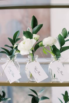 three vases with flowers are sitting on a shelf in front of a window and price tags hang from them