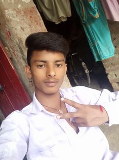 a young man standing in front of a building with his hand on his chest and pointing at the camera