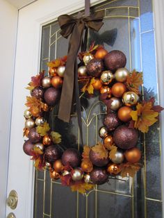 a wreath is hanging on the front door with autumn leaves and ornaments around it,