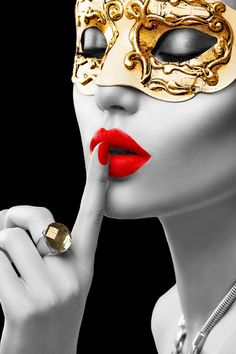 a woman wearing a gold mask and red lipstick with her finger to her lips,