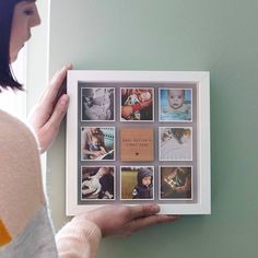 a woman is holding up a framed photo with photos on the wall in front of her