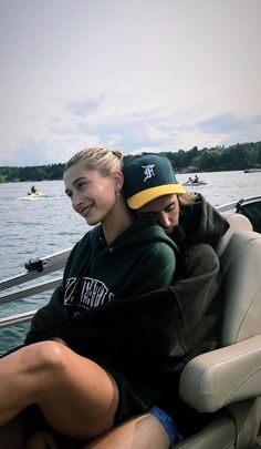 two people are sitting on a boat in the water and one is wearing a hat