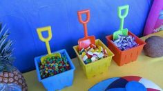 a table topped with plastic containers filled with candies and pineapples next to a blue wall