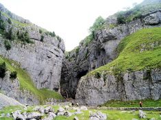 a man is standing in the middle of a rocky area with green grass and rocks