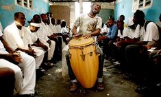 a man standing next to a large wooden drum in front of other men sitting down