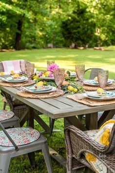 an outdoor table set with plates and glasses on it, surrounded by wicker chairs