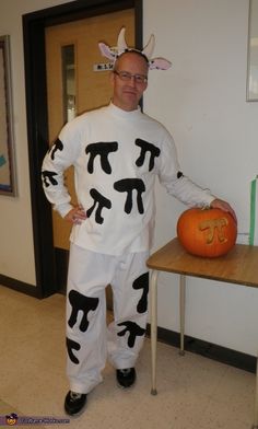 a man dressed up as a cow standing next to a table with a pumpkin on it