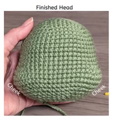 a hand holding a green crocheted hat on top of a wooden table