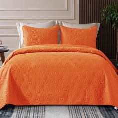 an orange bedspread with two pillows on top of it and a plant in the corner