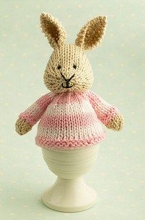 a knitted bunny in a pink and white sweater sitting on top of a cup