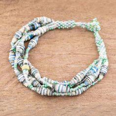 three strands of glass beads with green and white accents on a wooden surface, one strand is