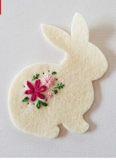 a white felt bunny with pink flowers on it's back and green leaves on its side