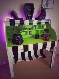 a green and white desk with black and white stripes on the bottom shelf, potted plants in front of it