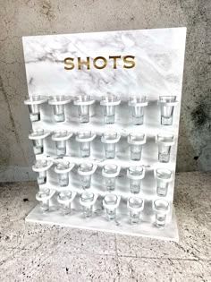 shot glasses are lined up on a marble display stand with the words shots in gold lettering