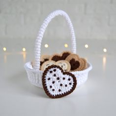 a crocheted basket filled with cookies on top of a white table next to lights