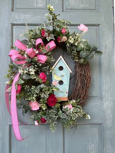 a wreath with a birdhouse and pink flowers hanging on the front door to decorate it