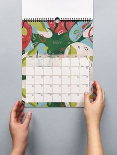 two hands holding up a calendar with an image of flowers on it and the date is may