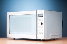 a white microwave oven sitting on top of a wooden table next to a blue wall