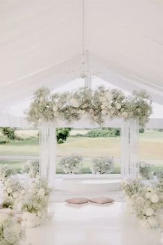 a white tent with flowers and pillows on the floor in front of a large window