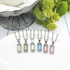 four necklaces with different colored stones sitting on a white plate next to some flowers