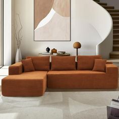 an orange couch sitting in front of a painting on the wall next to a stair case