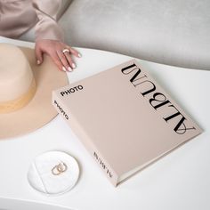 a woman's hand on the cover of a book next to a hat and ring