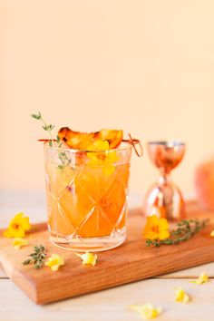 a glass filled with orange slices on top of a wooden cutting board next to flowers