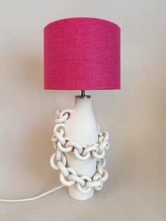 a white lamp with a pink shade on it sitting next to a red light plugged into the wall