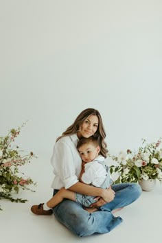 a woman sitting on the ground with her baby in her lap and flowers behind her