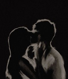 a black and white photo of a man kissing a woman's head in front of a dark background