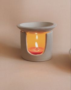 a small white candle holder with a red lit candle in the center on a beige background