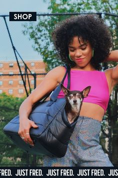 Young black stylish female holding a black puffer like fabric dog carrier with a small dog peeking its head out.  Shop at JUST FRED