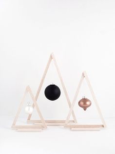 three ornaments are placed in triangle shapes on wooden stands against a white wall, one is black and the other is gold